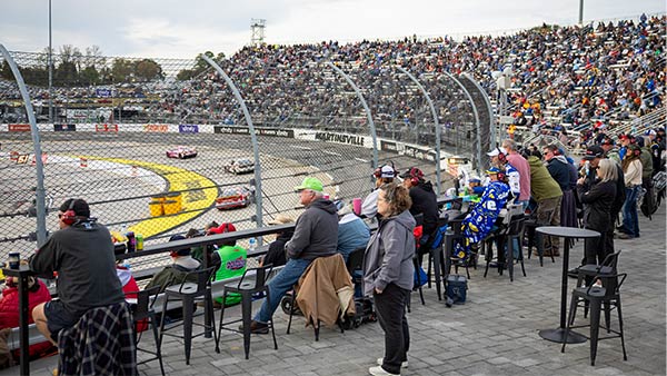 Spectators seated at trackside bar tables watch the race cars pass by on the Martinsville short track.